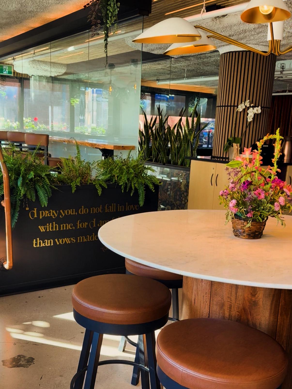 Cafe X interior with plants, round table, and brass lighting
